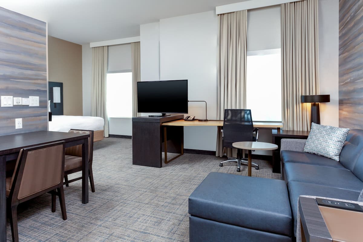 Ett hotellrum med en säng, ett skrivbord med en dator, en tv, en soffa och ett litet bord.