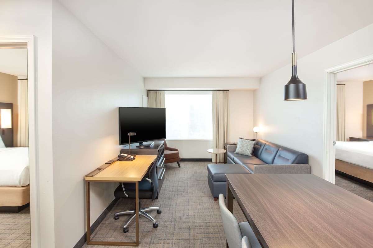 Ett hotellrum med en säng, ett skrivbord med en dator, en tv, en soffa och ett matbord.