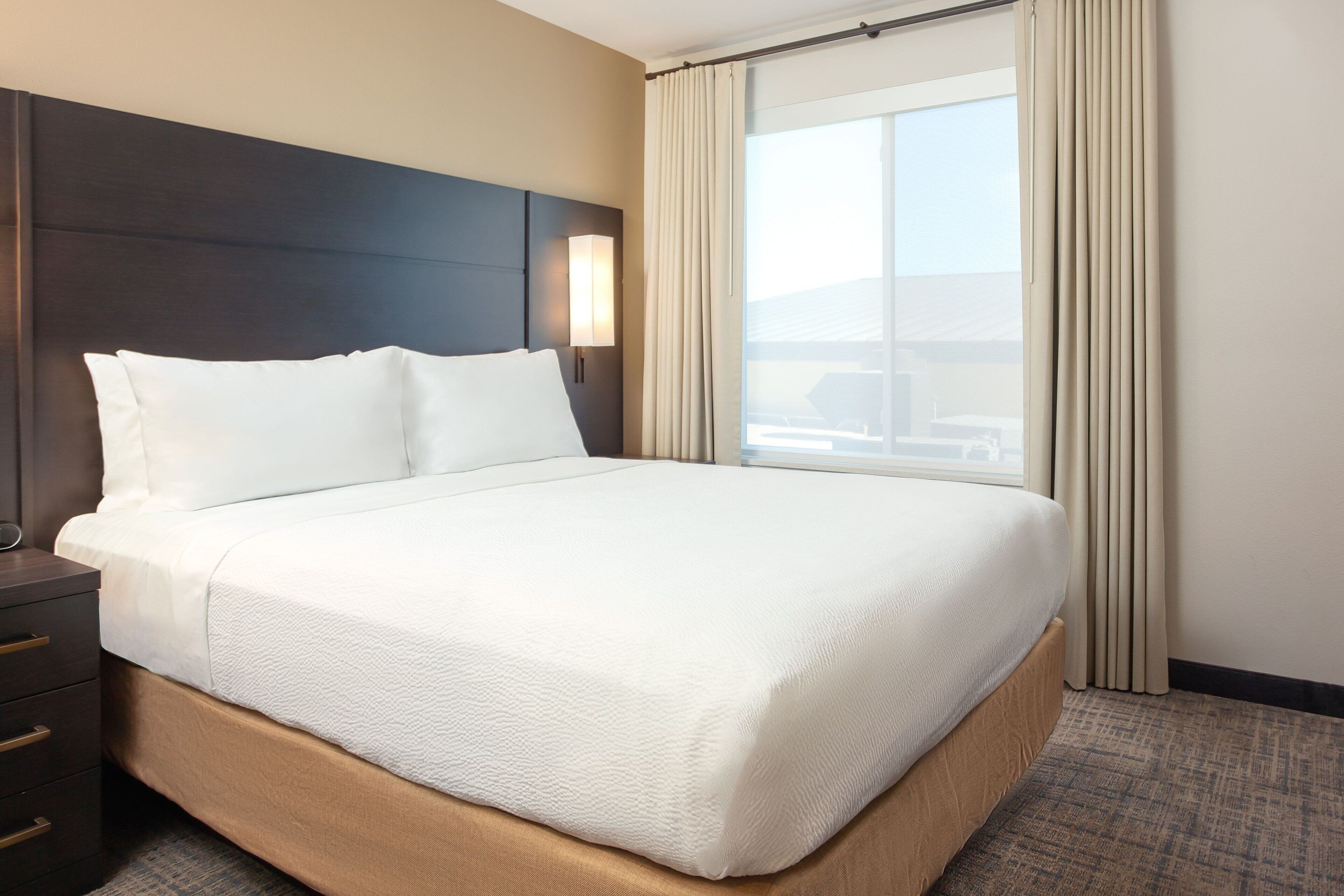 A hotel room with a large bed, a nightstand, a lamp, and a window with curtains.