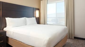 A hotel room with a large bed, a nightstand, a lamp, and a window with curtains.