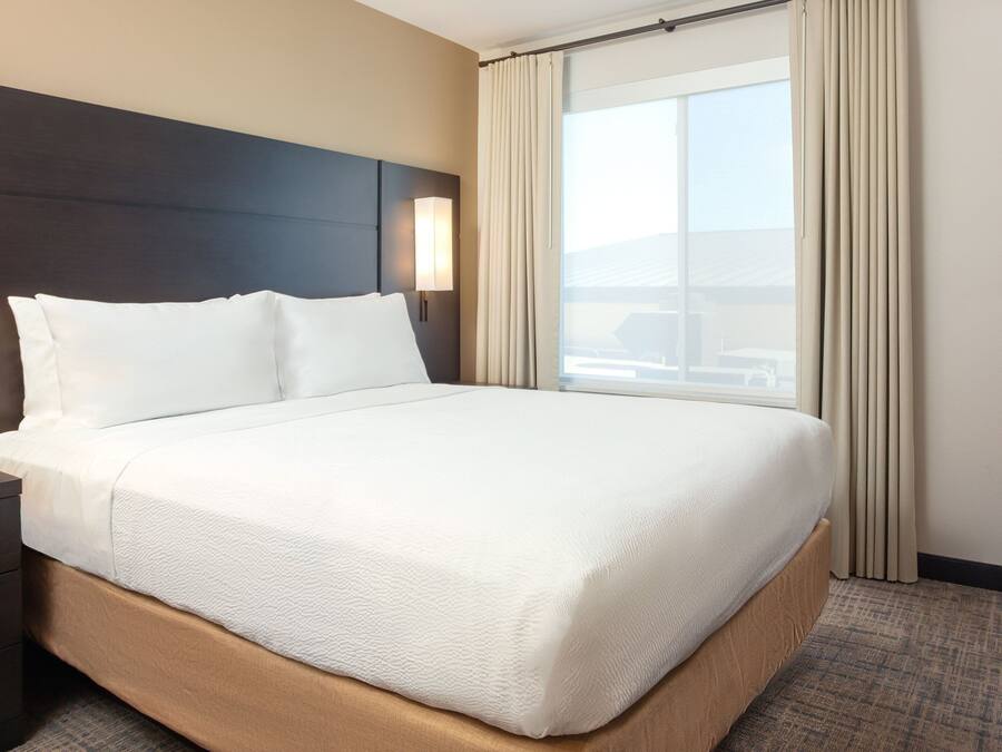 A hotel room with a large bed, a nightstand, a lamp, and a window with curtains.
