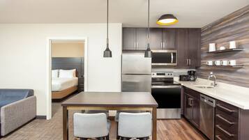 A compact hotel room with a kitchenette, a dining area with two chairs, a bed, and a small seating area.