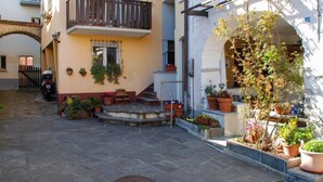 Un cortile con pavimento in pietra, uno scooter parcheggiato all'esterno e piante in vasi sui gradini.