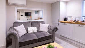 Ein modernes Wohnzimmer mit grauem Sofa, einem Couchtisch und einer Küchenzeile mit weißen Schränken und einer Holzarbeitsplatte.