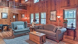 A spacious wooden cabin interior with a high ceiling, multiple windows, a staircase, and a cozy seating area with a sofa and armchairs. - Views high above the river with a pleasant walk to Midtown shops and food. (Ruidoso)