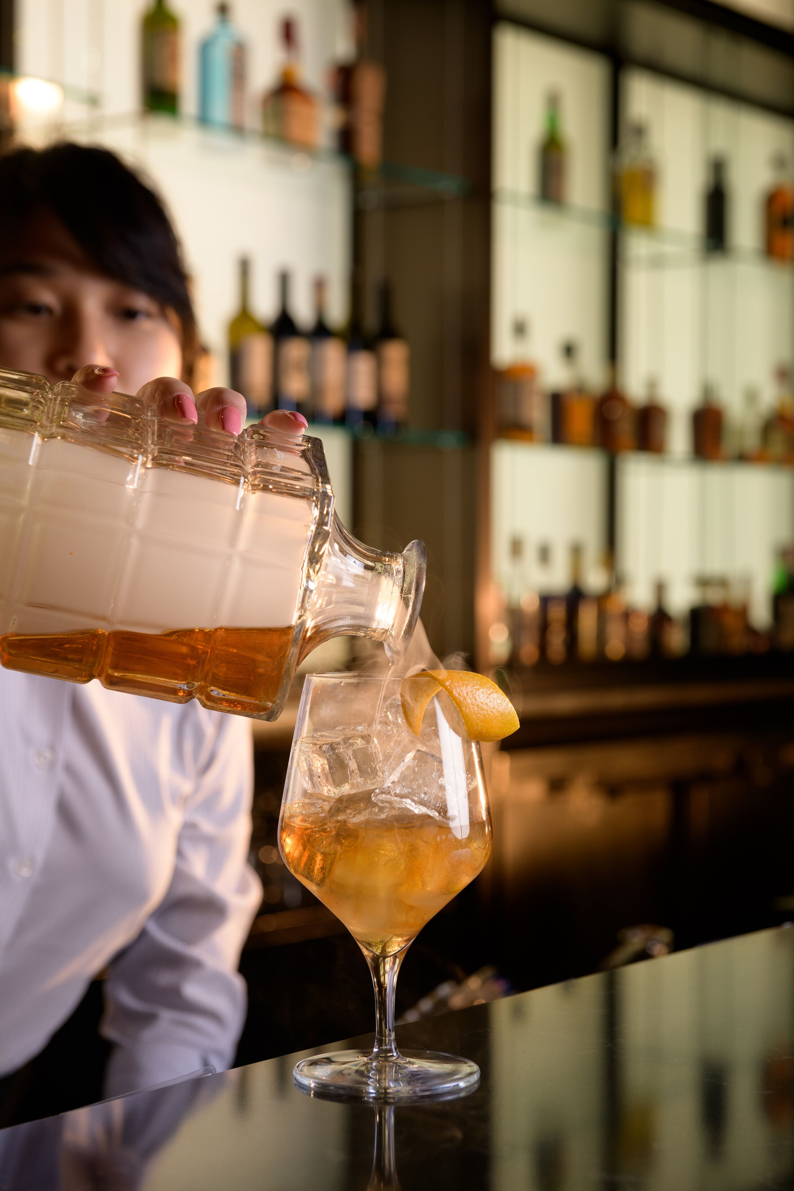 Een barman schenkt een drankje in een glas met een citroenpartje.