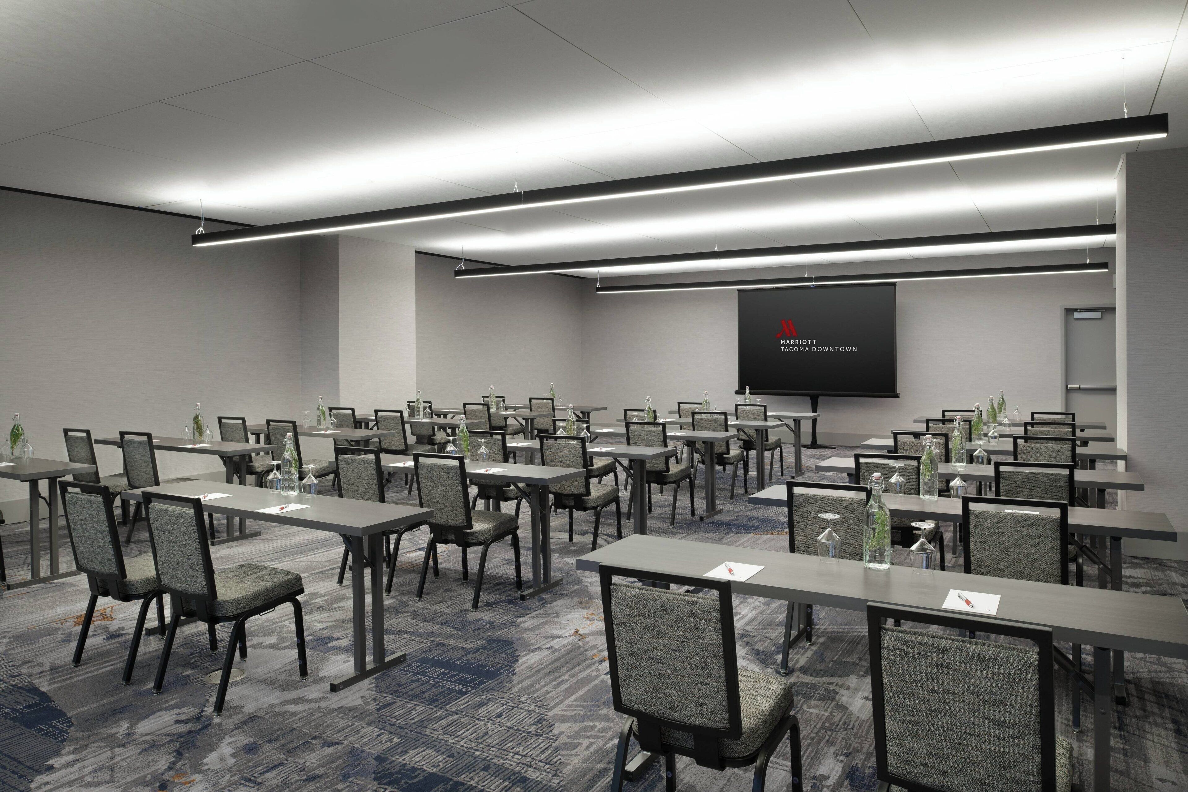 A conference room with multiple tables and chairs, a projector screen, and a carpeted floor.