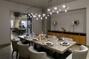 A modern dining area with a long table set for a meal, featuring a mix of chairs and a bar area.