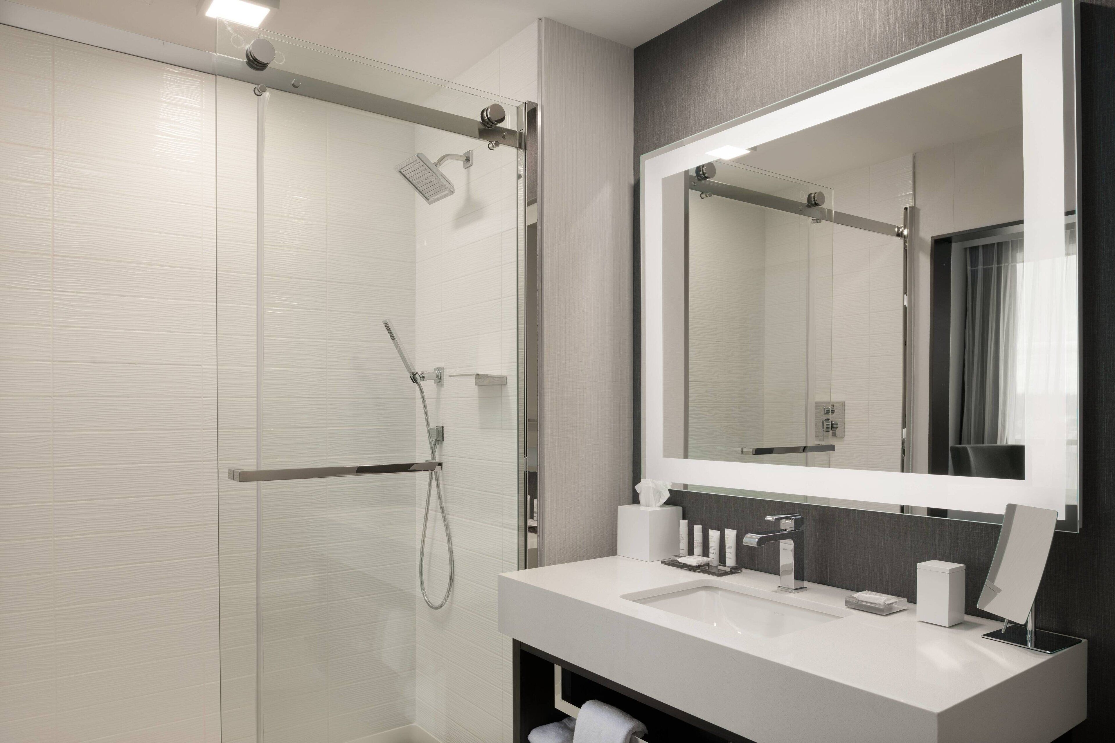 Un baño moderno con cabina de ducha de vidrio, un espejo grande y un lavabo blanco con encimera.