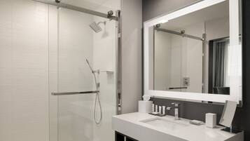 Un baño moderno con cabina de ducha de vidrio, un espejo grande y un lavabo blanco con encimera.