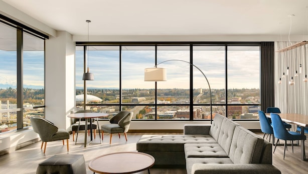 A modern living room with a large window, a sofa, a dining table, and chairs. - Marriott Tacoma Downtown (Tacoma)
