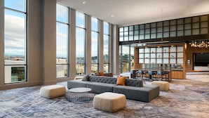 A spacious lounge area with a large gray sofa, ottomans, and a round coffee table. A bar area with stools is visible in the background. - Marriott Tacoma Downtown (Tacoma)