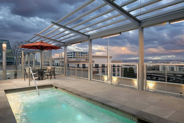 A rooftop pool with a glass enclosure, outdoor seating, and a city view.