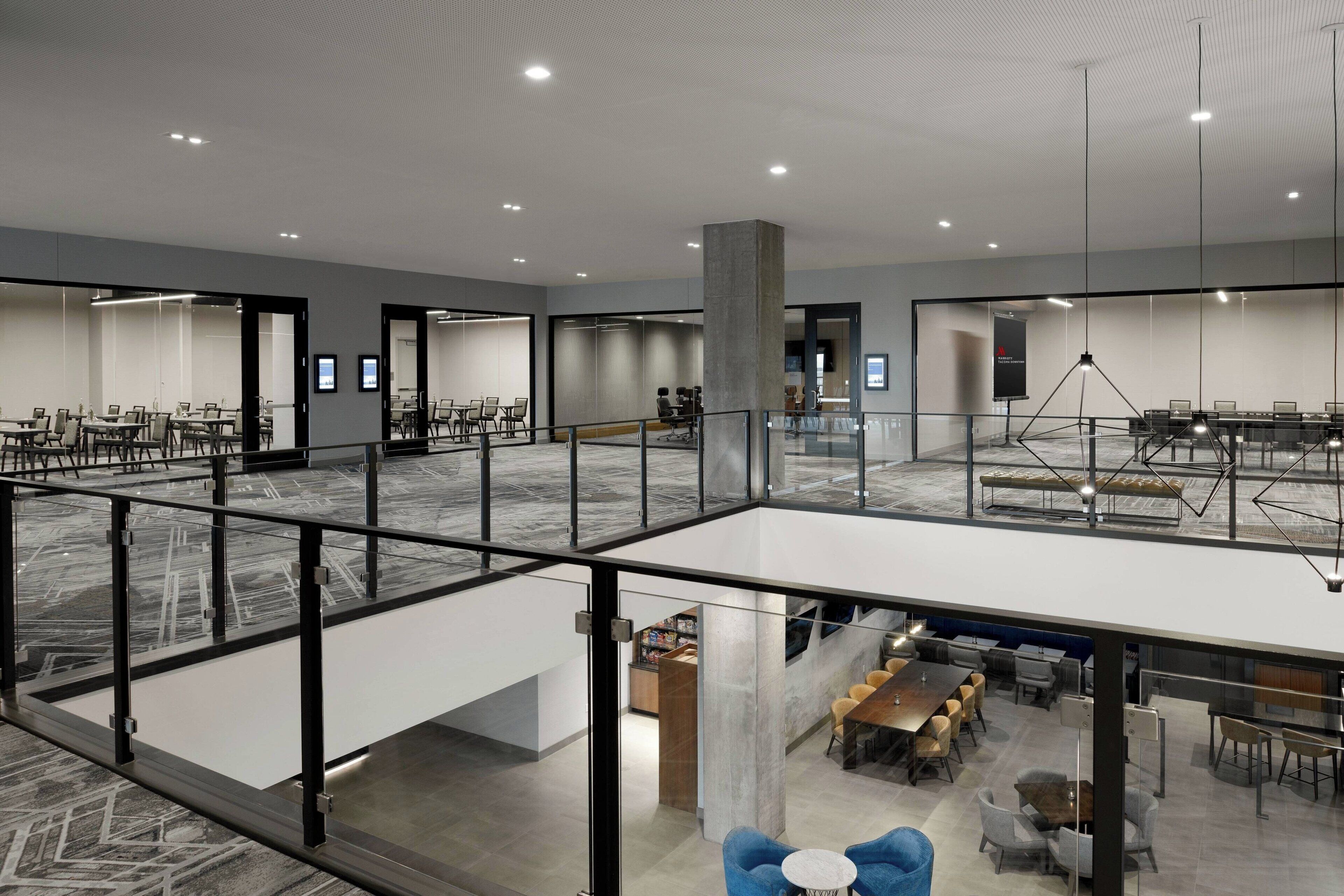 Une salle de conférence spacieuse et moderne, dotée de murs en verre, d’un plafond haut et d’une mezzanine aménagée avec des sièges.