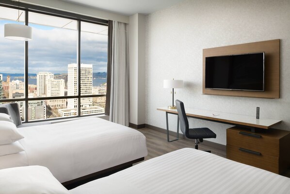 Habitación de hotel con dos camas, un escritorio, una silla, un televisor y vista a la ciudad.