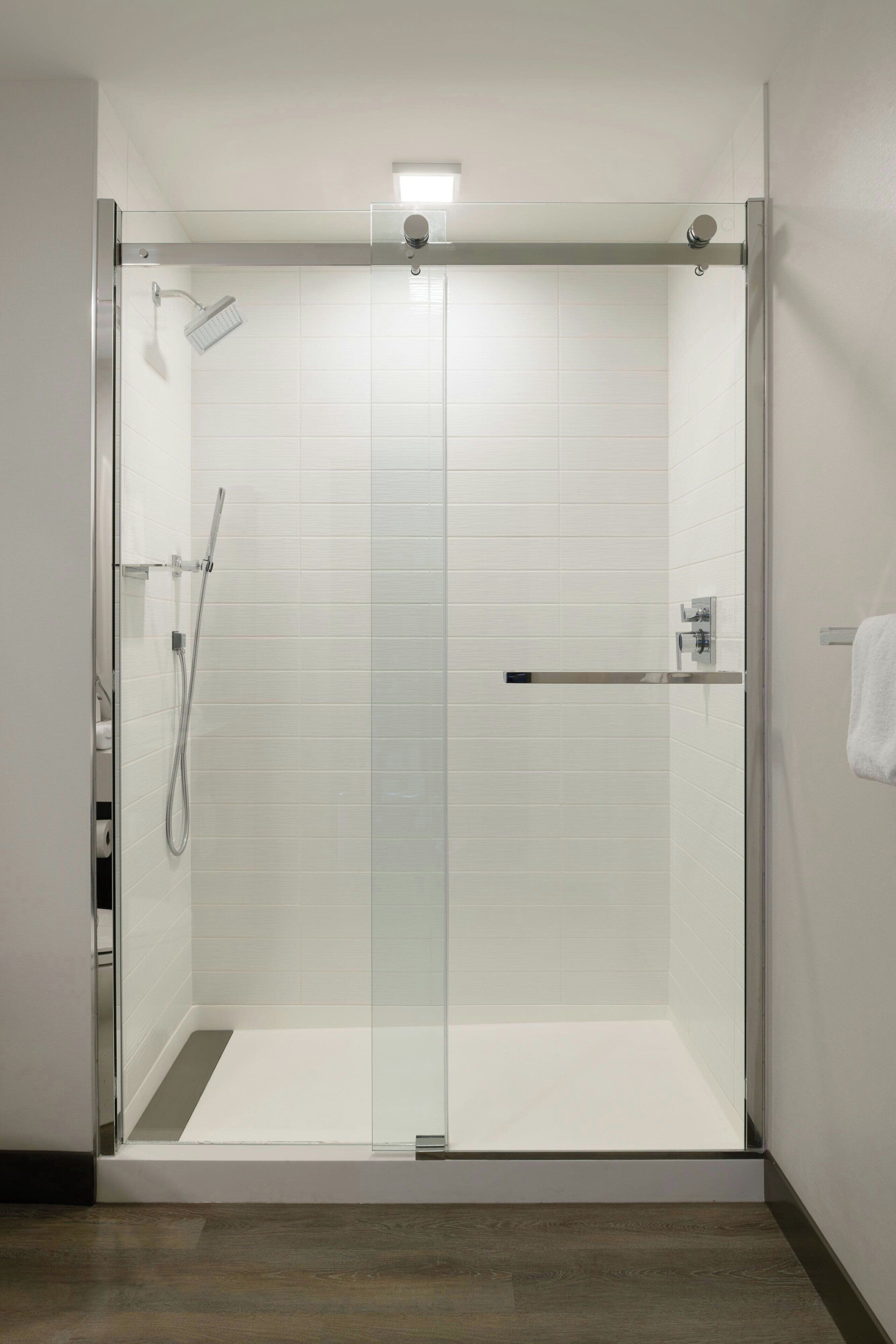 A modern shower enclosure with a glass door, a handheld showerhead, and a control panel.