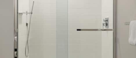 A modern shower enclosure with a glass door, a handheld showerhead, and a control panel.