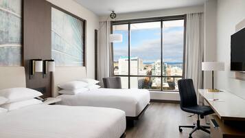 A hotel room with two beds, a desk, a chair, a TV, and a large window with a city view.