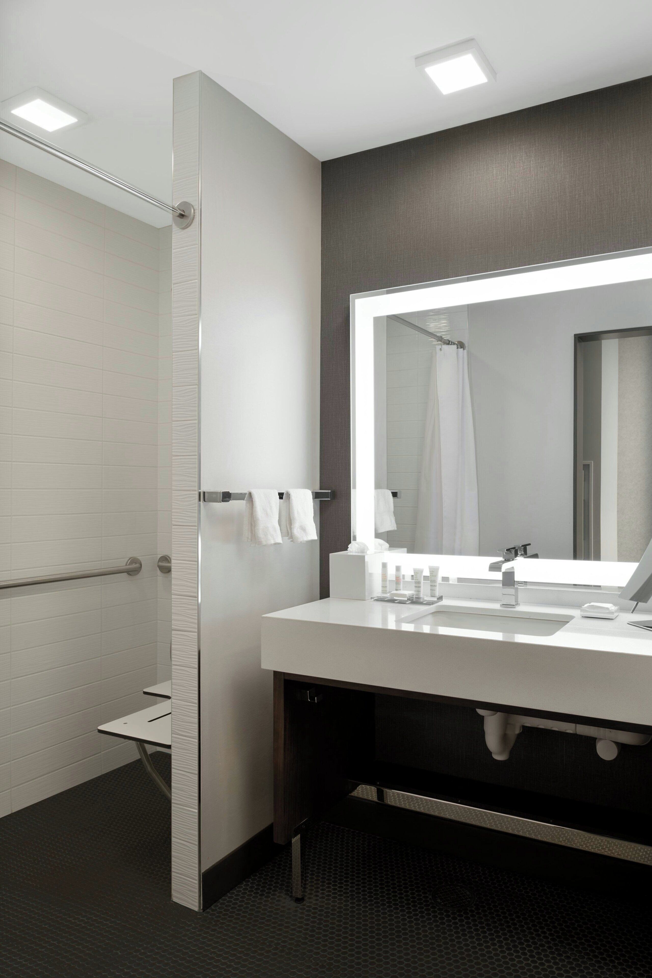 A modern bathroom with a walk-in shower, a large mirror, and a vanity with a sink and towel rack.