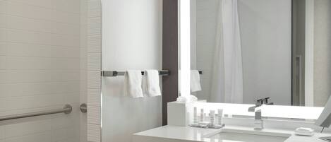 A modern bathroom with a walk-in shower, a large mirror, and a vanity with a sink and towel rack.