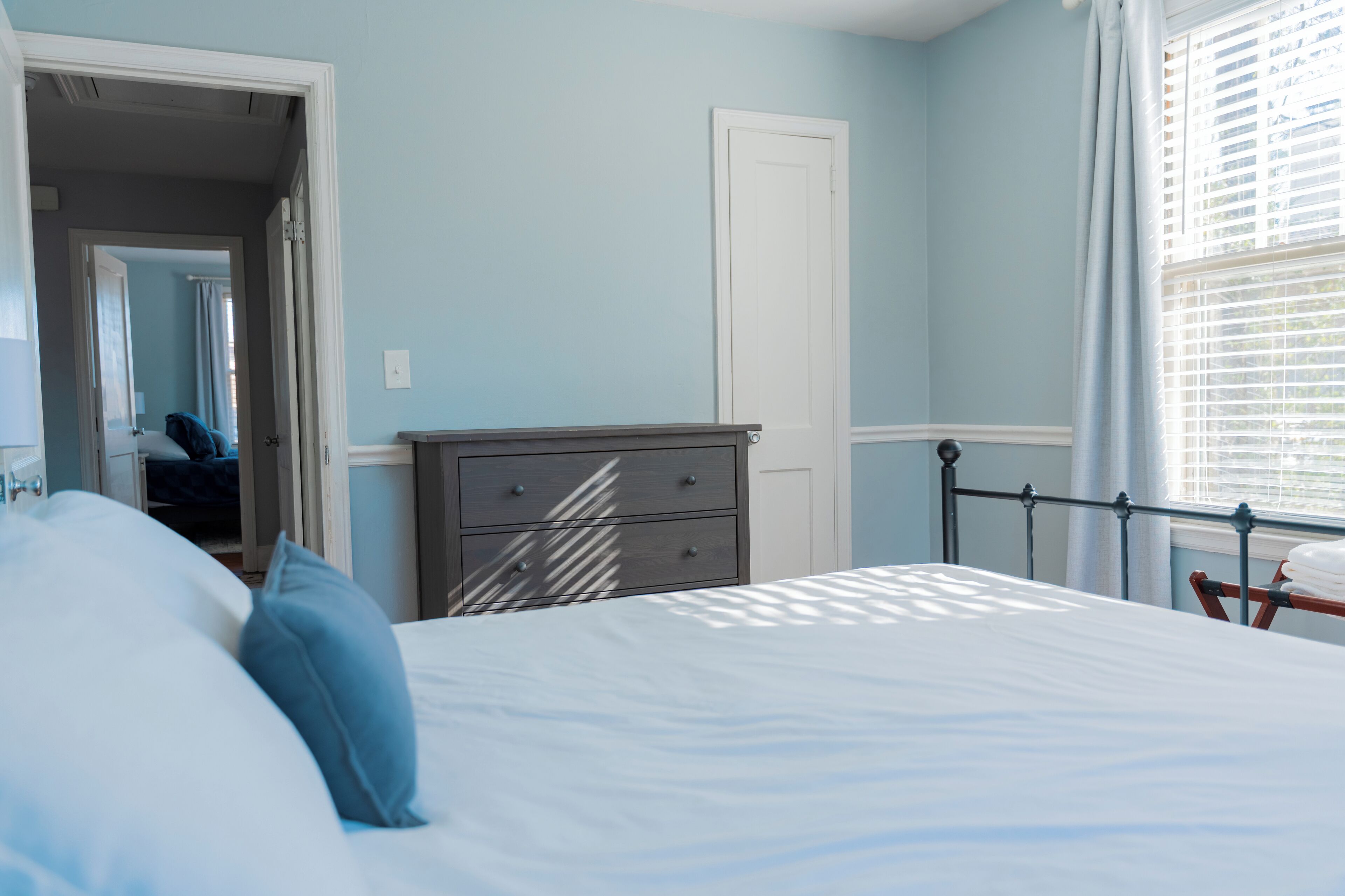 A bedroom with a bed, a dresser, a door, and a window with blinds.