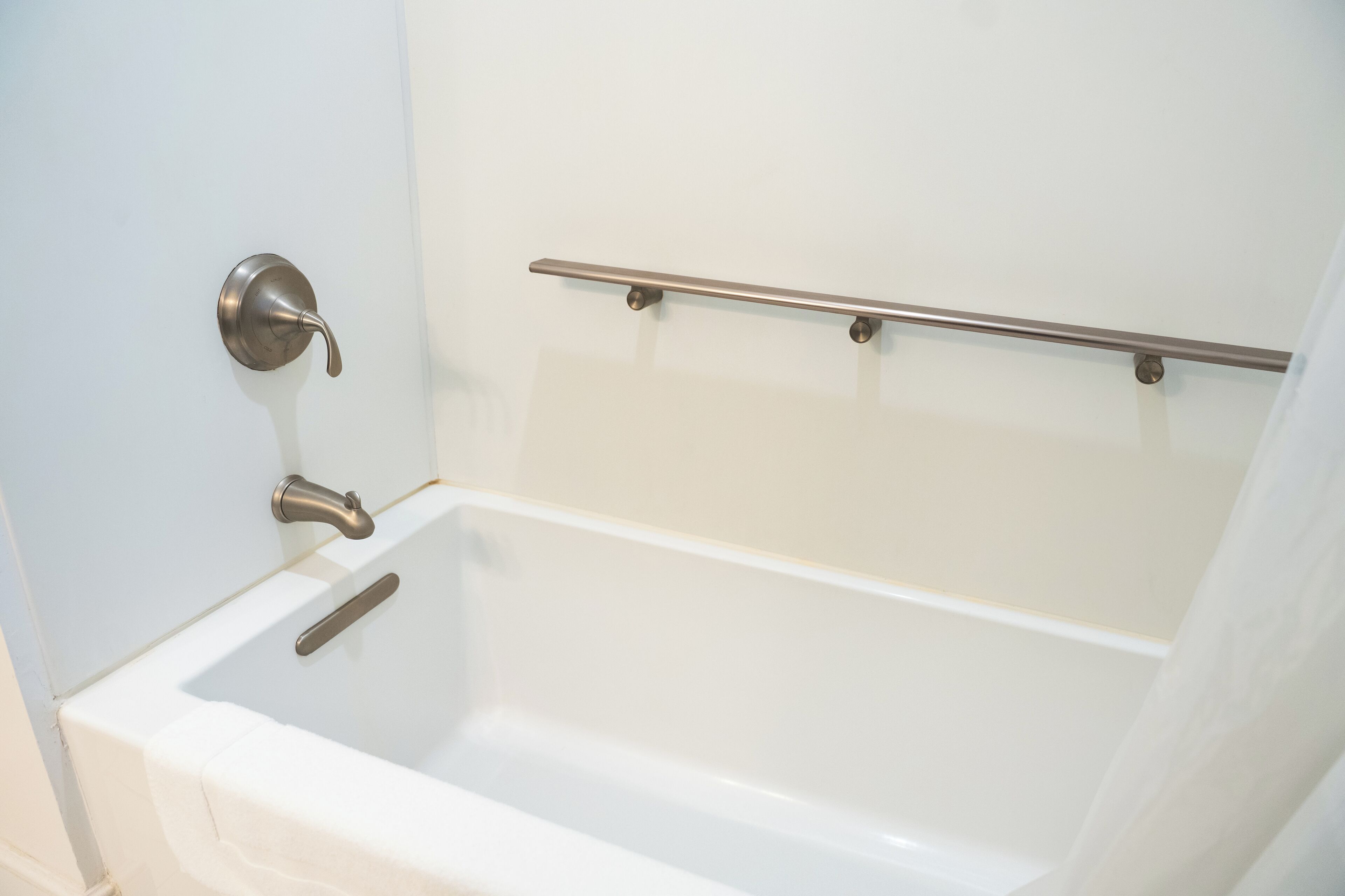 A white bathtub with a chrome faucet and a chrome grab bar.