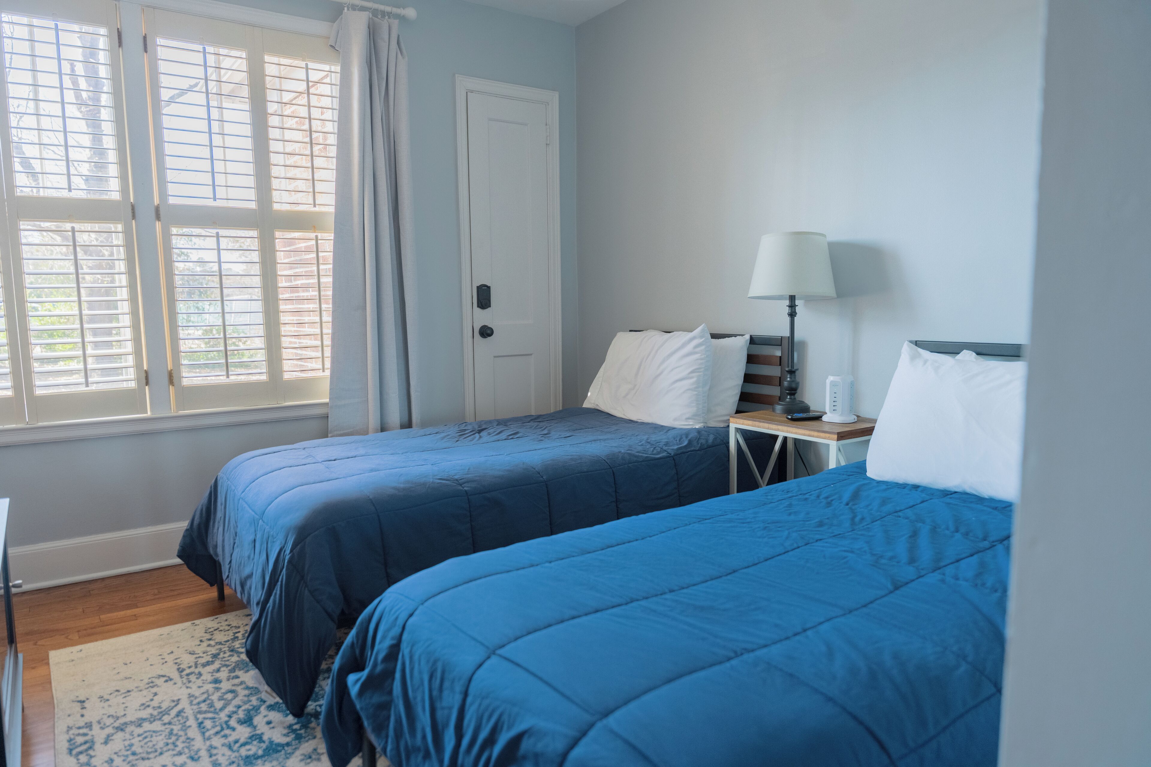 A room with two beds, a nightstand, a lamp, and a window with blinds.