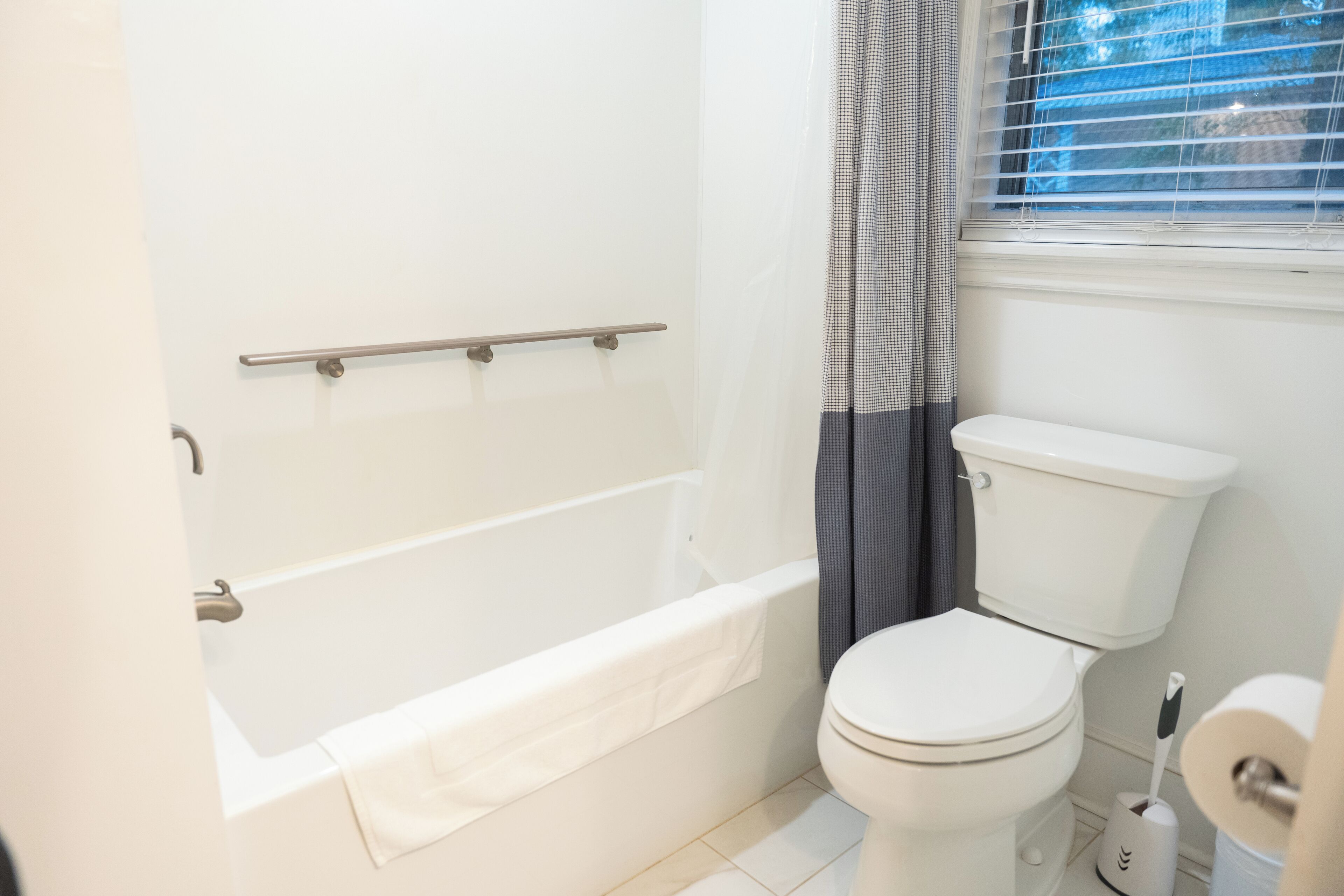 Une salle de bain avec une baignoire, des toilettes et une fenêtre avec des stores.