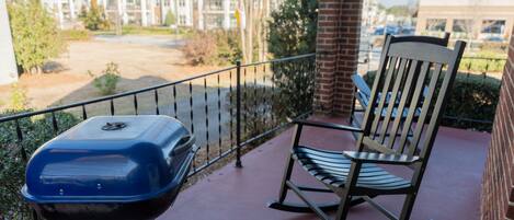A balcony with a grill, a rocking chair, and a view of apartment buildings.