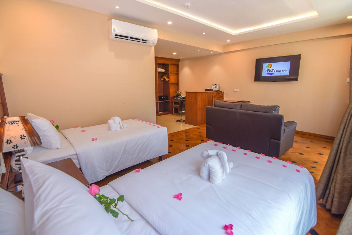 A hotel room with two beds, a sofa, a TV, and an air conditioning unit.