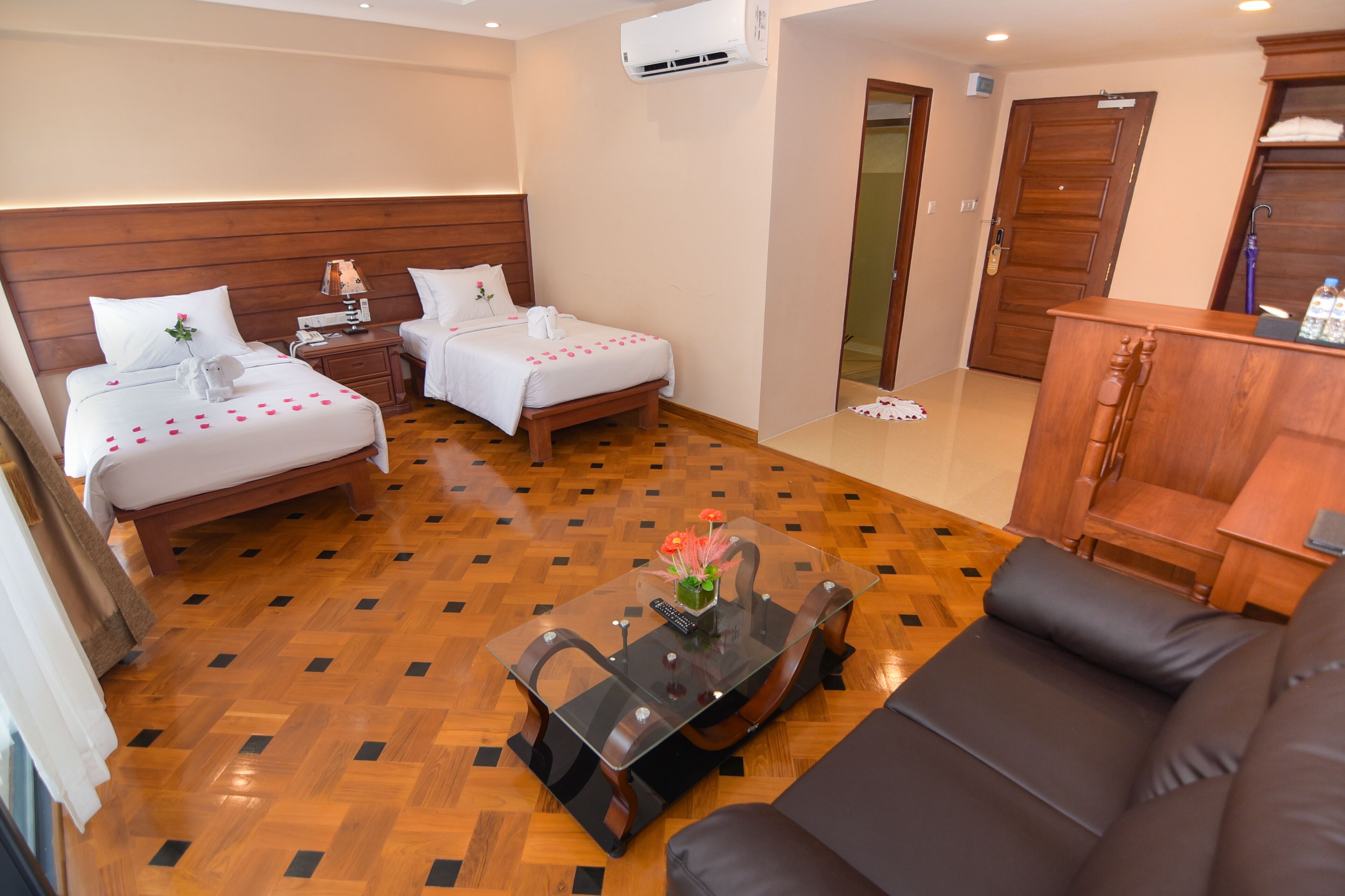 A hotel room with two beds, a sofa, a glass coffee table, and a wooden cabinet.