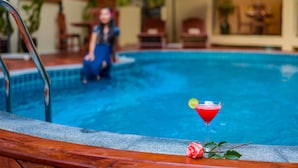 Une piscine avec une terrasse en bois et un verre de cocktail rouge garni d’une tranche de citron.