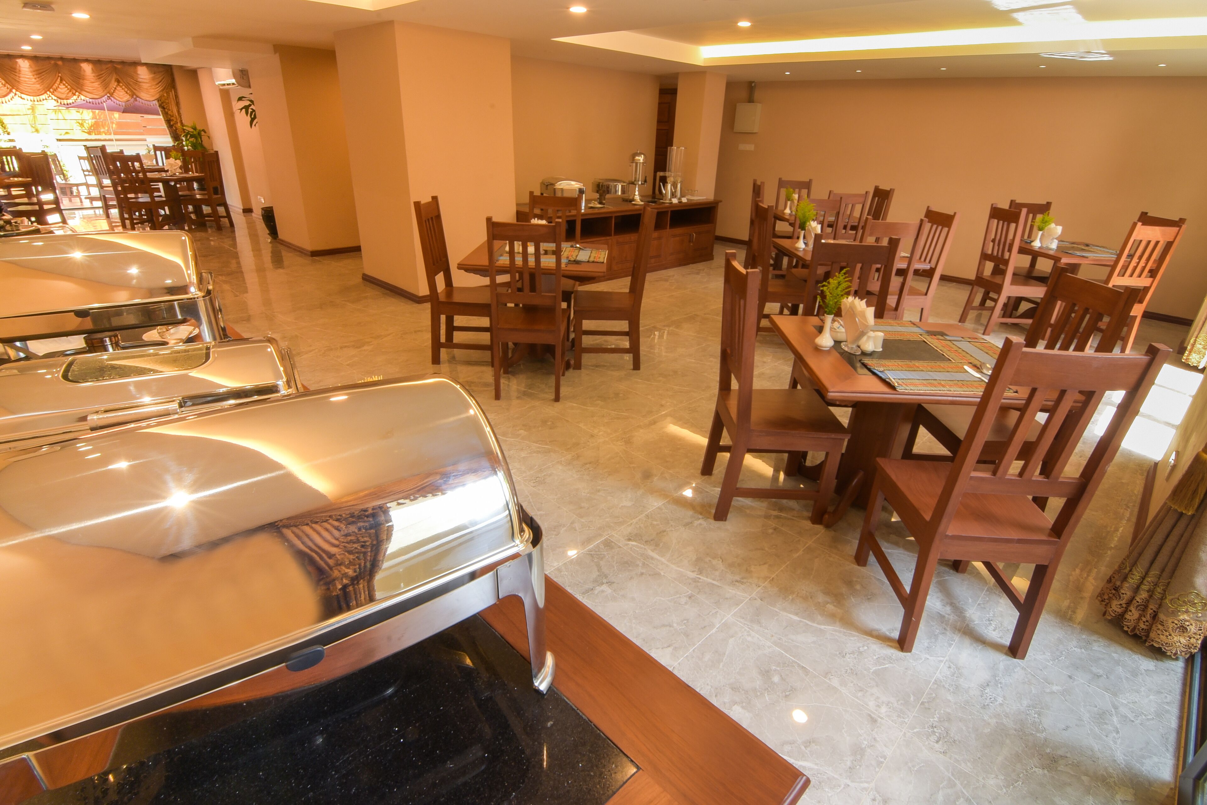 A spacious dining area with multiple wooden tables and chairs, a central island with kitchen appliances, and a large vehicle parked in the foreground.
