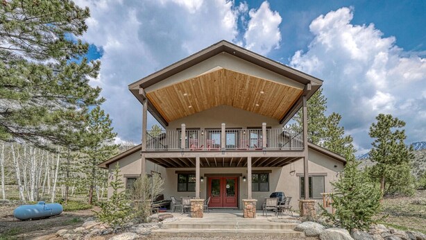 Une maison à deux étages avec une terrasse en bois et une porte rouge.