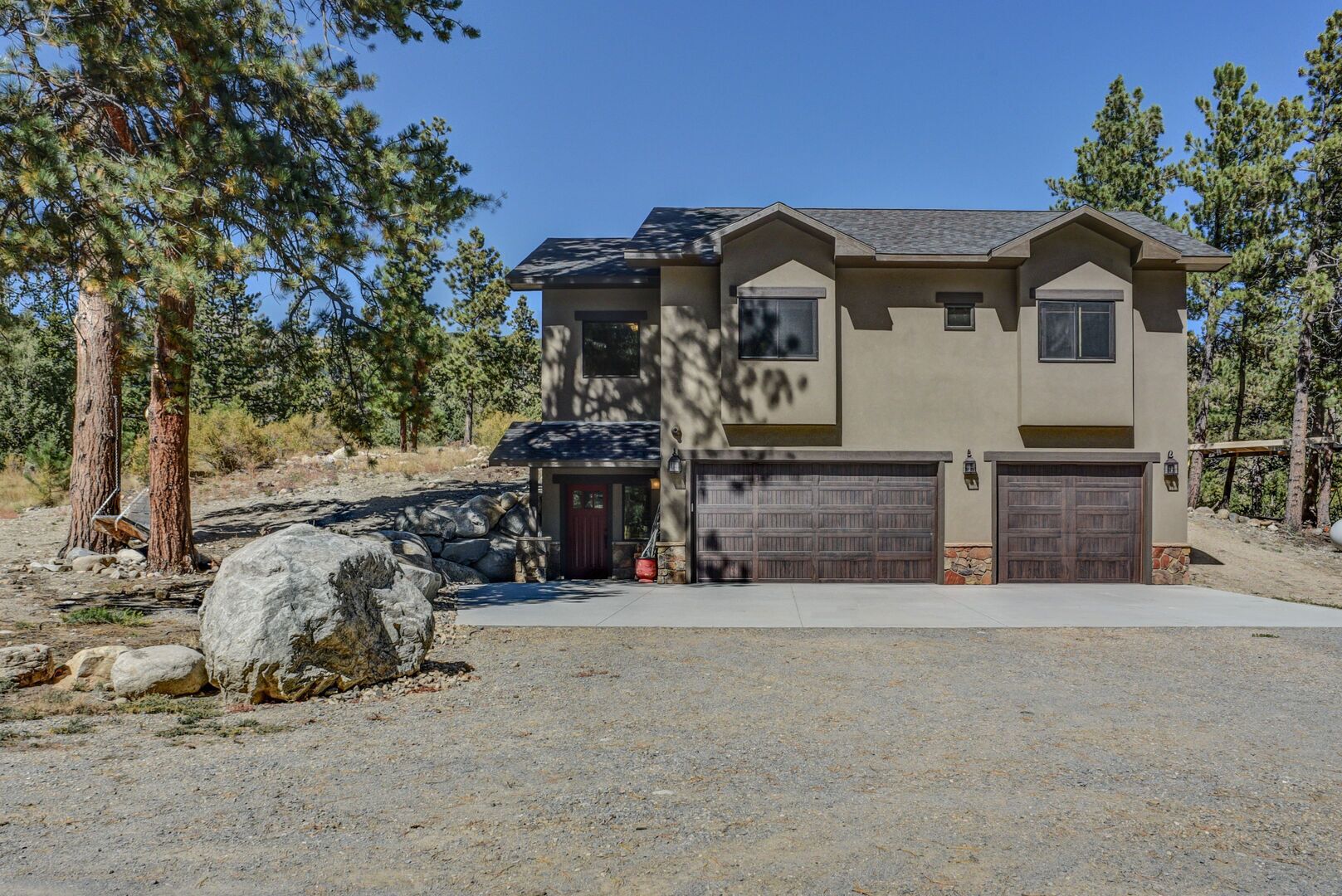 A two-story house with a garage, surrounded by trees and a rocky landscape.
