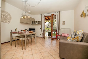 A dining area with a table and chairs, a sofa, and a view through an open door to an outdoor space.