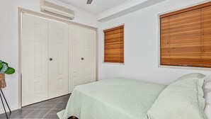 Un dormitorio con cama, armario y dos ventanas con persianas de madera.