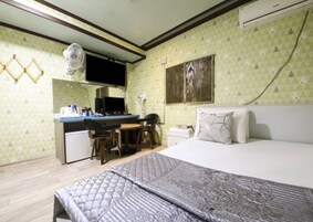A bedroom with a bed, a desk with a computer, a chair, and a small table.