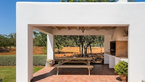 A covered outdoor area with a wooden bench, a brick grill, and a potted plant. - Beautiful Villa “Sa Vinyeta” with Mountain View, Air Conditioning, Pool & Terrace (Sant Joan de Labritja)