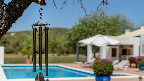 A pool area with a wind chime, lounge chairs, and a potted plant. - Beautiful Villa “Sa Vinyeta” with Mountain View, Air Conditioning, Pool & Terrace (Sant Joan de Labritja)