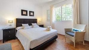 A bedroom with a bed, nightstands, a chair, a window with curtains, and framed pictures on the wall. - Beautiful Villa “Sa Vinyeta” with Mountain View, Air Conditioning, Pool & Terrace (Sant Joan de Labritja)