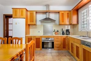 Een keuken met houten kastjes, een Bosch koelkast, een oven en een spoelbak.