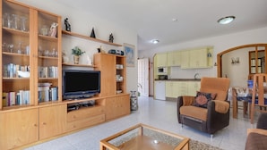Una sala de estar con televisor, estanterías, una mesa de centro y un comedor con una silla y mesa.
