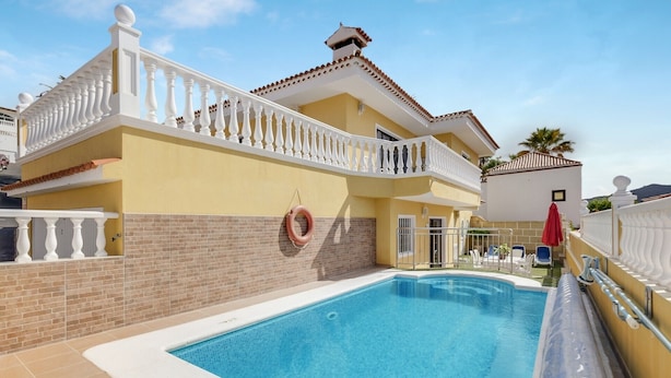 Una piscina con barandilla blanca, un flotador salvavidas y un paraguas rojo.