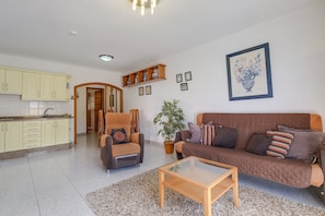 Uma sala de estar com sofá, poltrona, mesa de centro e um vaso de planta.