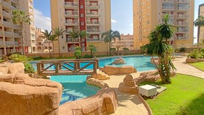 A swimming pool with rock formations and palm trees, surrounded by apartment buildings. - One bedroom apartment in Veneziola (La Manga del Mar Menor)