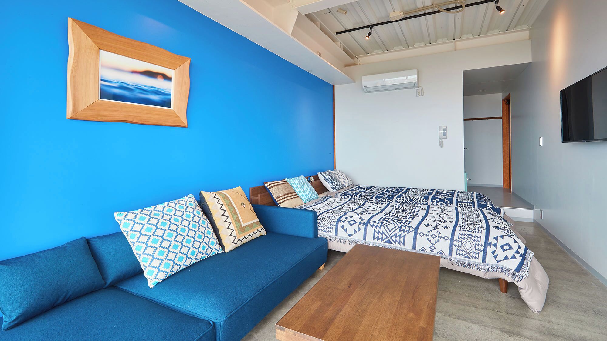 Ein modernes Zimmer mit blauer Wand, einem Bilderrahmen aus Holz, einem blauen Sofa, einem bettenförmigen Muster und einem Holztisch.