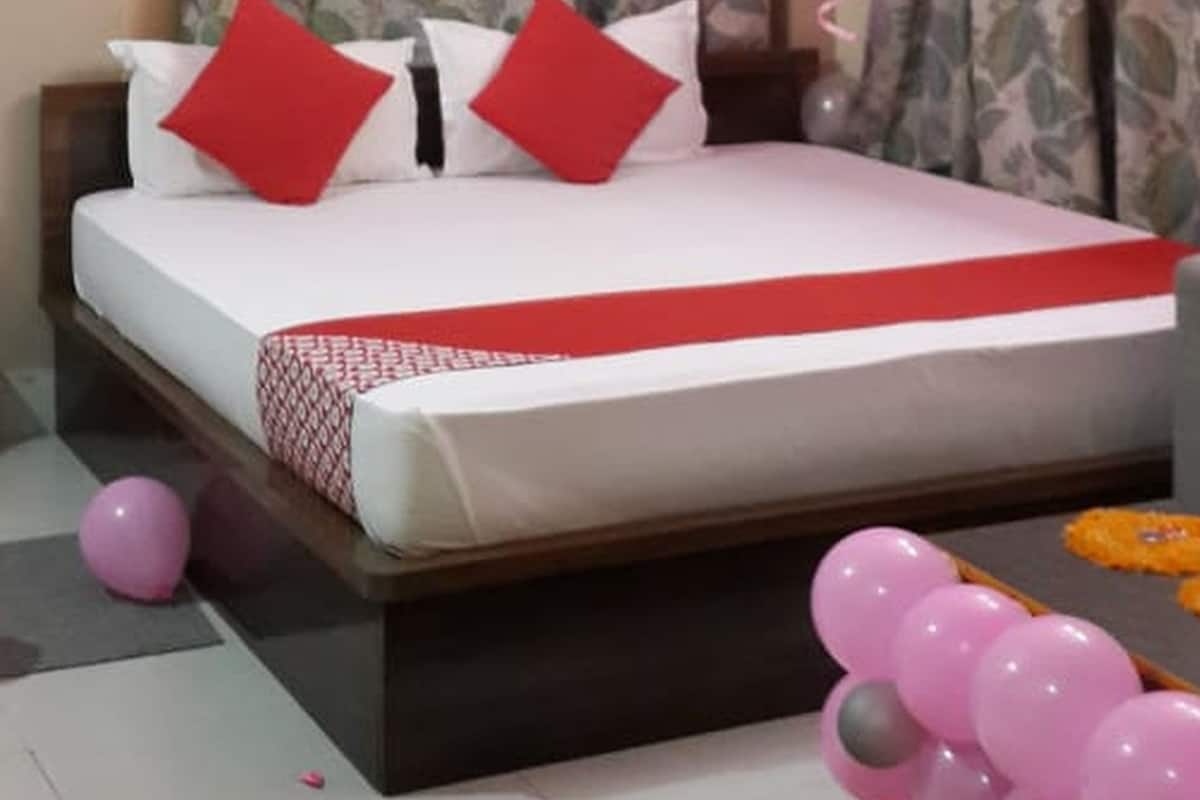 Una cama bien hecha con una colcha blanca y roja, almohadas rojas y un adorno de globo rosa en el suelo.