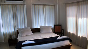 A hotel room with a large bed, two bedside tables, a chair, and a window with curtains. - Hotel Greenwood (Siliguri)