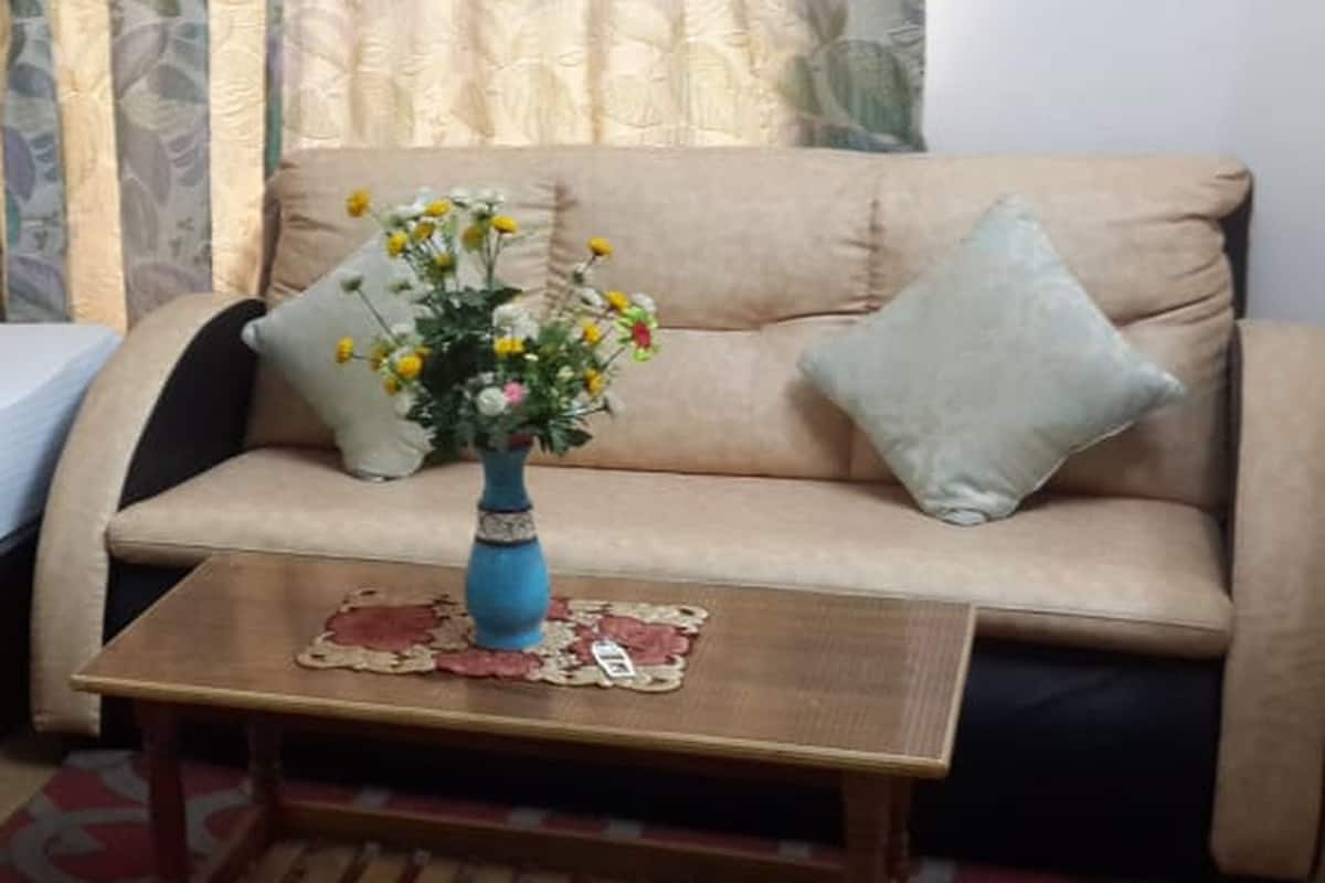 Una sala de estar con un sofá color beige, un jarrón azul con flores y una mesa de centro de madera.